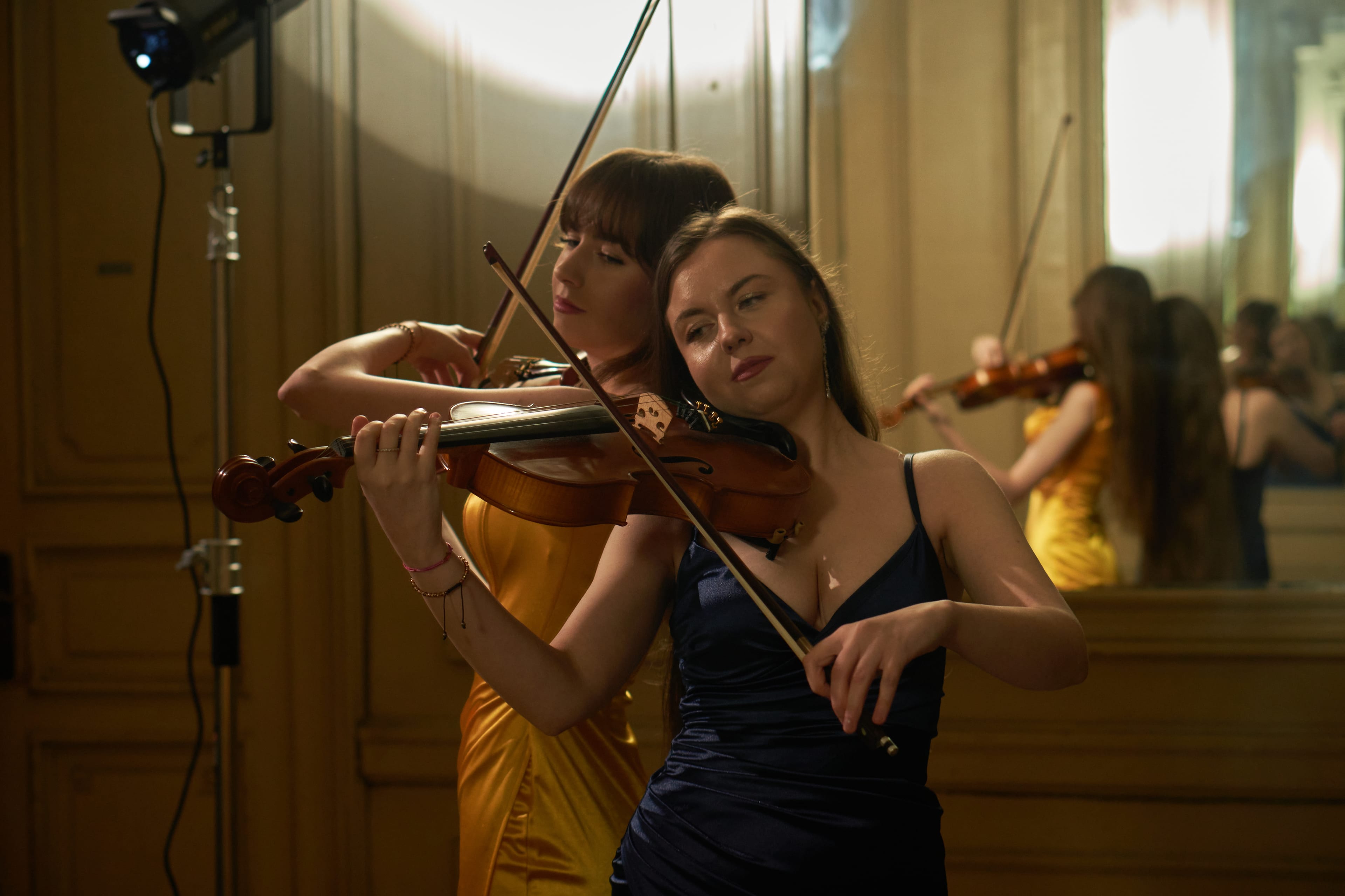 Duo-ul Sistrings stând spate în spate, în rochii roșie și neagră, cu vioară și violă